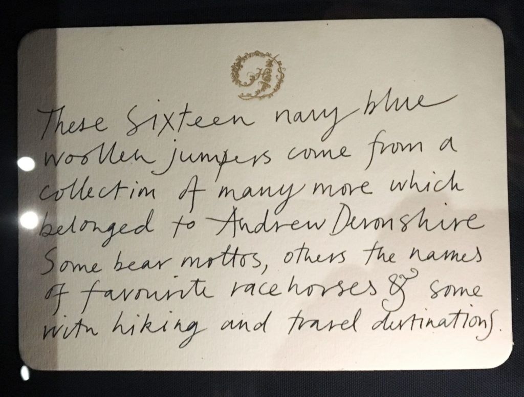 A hand written label saying " These sixteen navy blue woollen jumpers come from a collection of many more which belonged to Andrew Devonshire, some bare mottos, others the names of favourite race horses and some with hiking an travel destinations