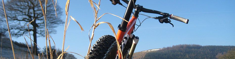 A close up of a section of a mountain bike, with its thick tyres, with blue skies and the tops of rolling Derbyshire hills in the background