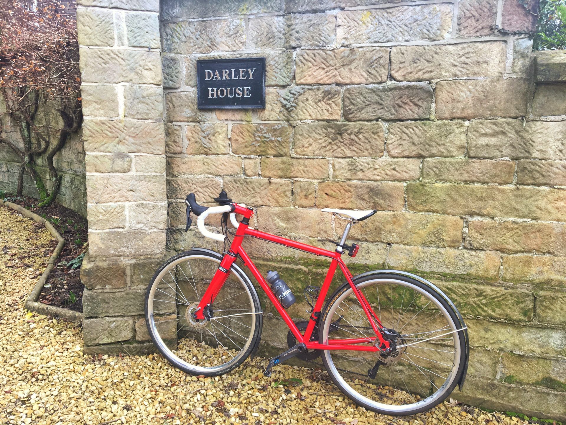 A red road bike propped up against the stone wall showing the Darley House name sign